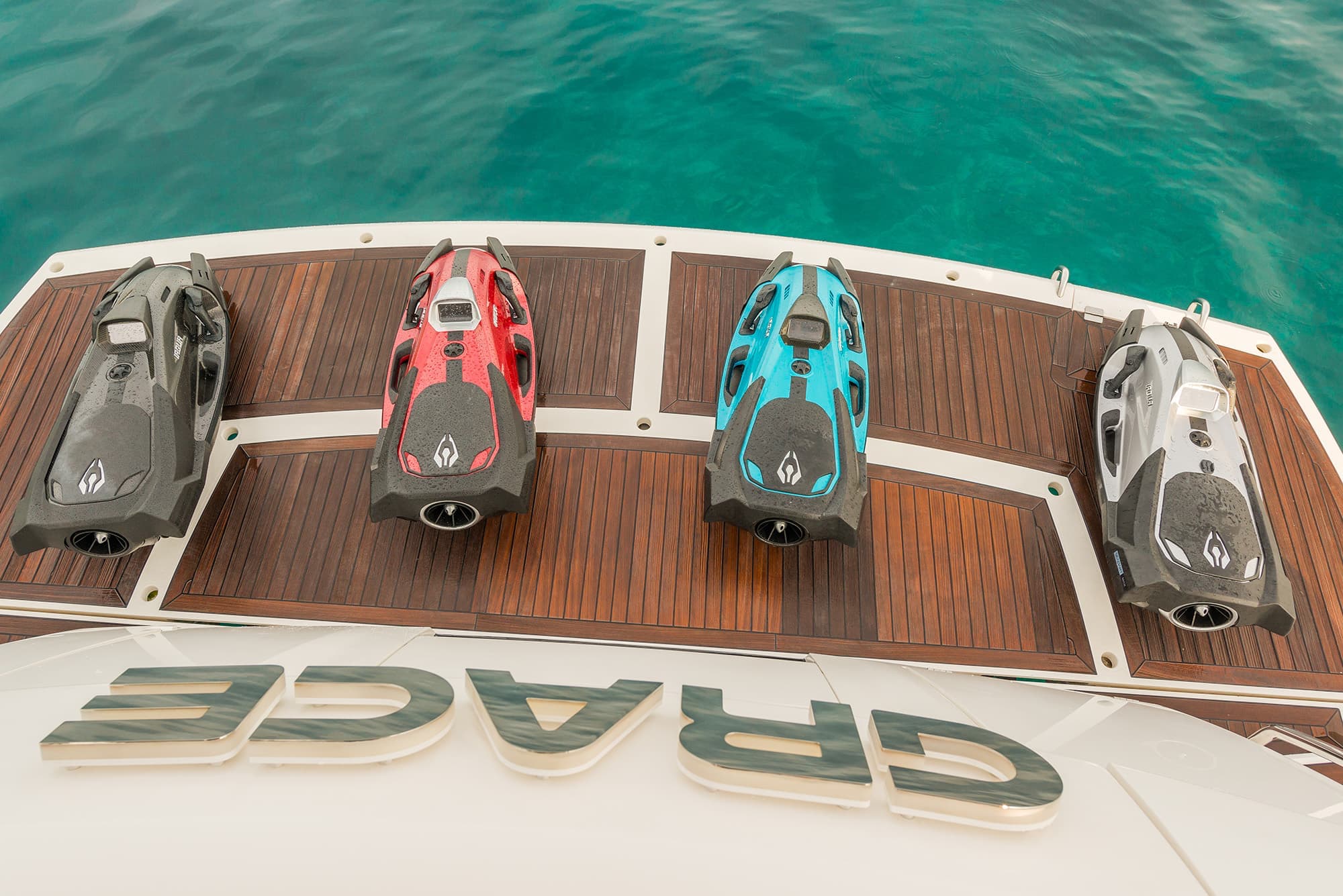 Four scuba jets in black, red, blue, and grey are lined up on a wooden deck.